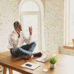 Young african-american man doing yoga at home while being quarantine and freelance working